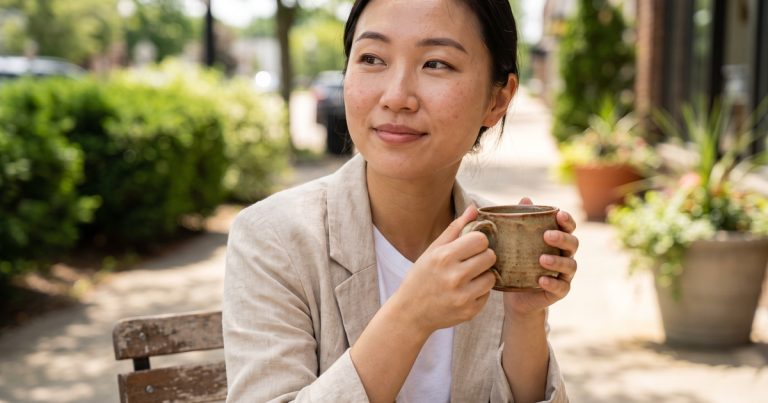 A woman pauses over coffee at a sidewalk cafe table, feeling steadier as TMS for depression takes hold in Portage, MI.